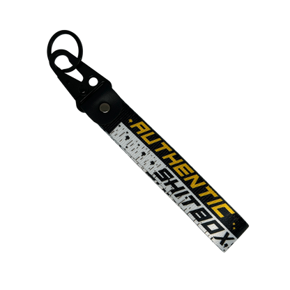 Back side of a black, white and yellow keychain with gritty design reading "Authentic Sh*tbox" – Motorev automotive keychain accessory